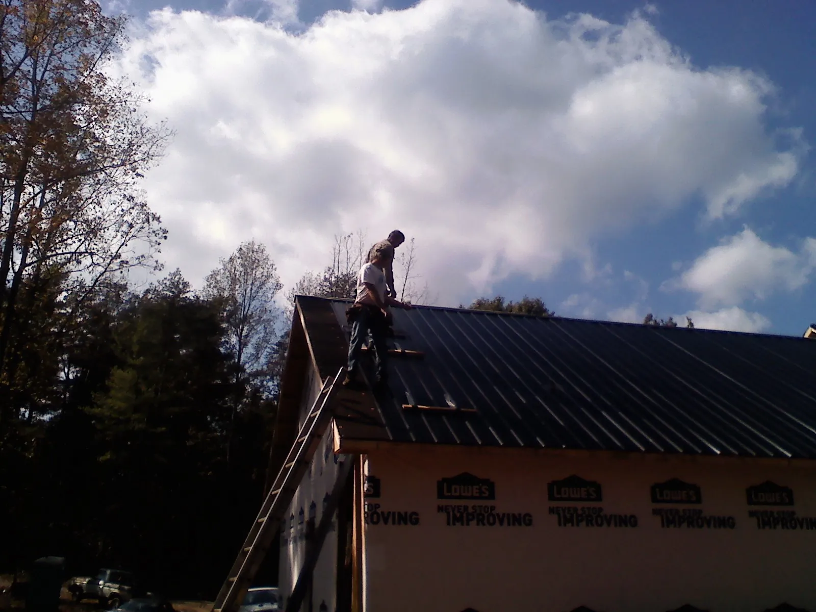 Roofer fastening dark metal panels high against a cloudy sky, from a Roof Inspection job in Lewisville